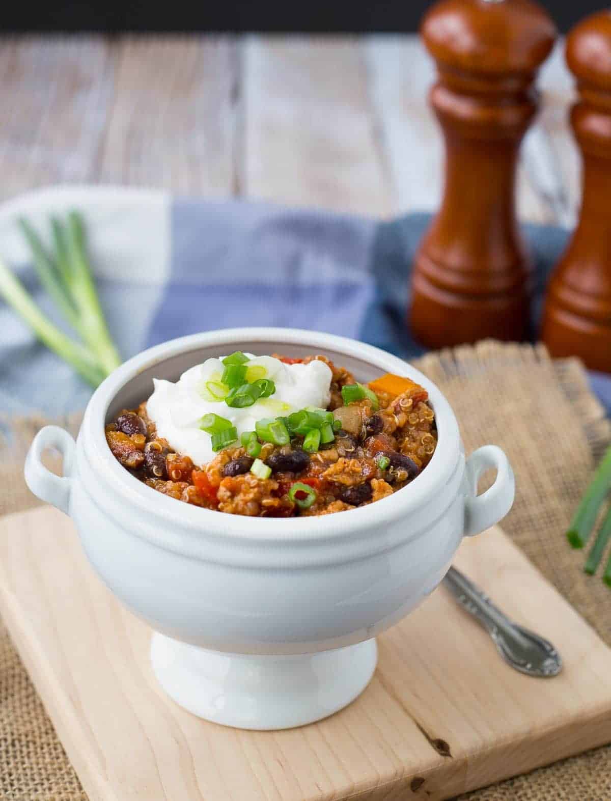 Serving of chili in white footed ball garnished with sour cream and sliced green onion.