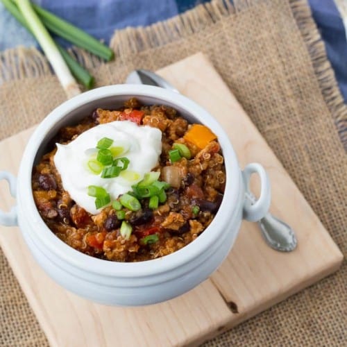 Quinoa chili in white bowl garnished with sour cream and green onions.