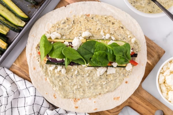 Baby spinach leaves laid over roasted vegetables and feta in the middle of a tortilla wrap.