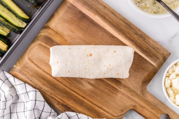 A rolled veggie wrap on a wooden cutting board.