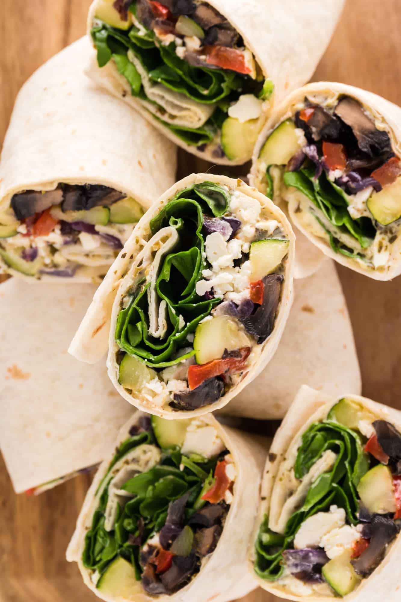 Assorted halves of roasted vegetable wraps on a wooden cutting board.