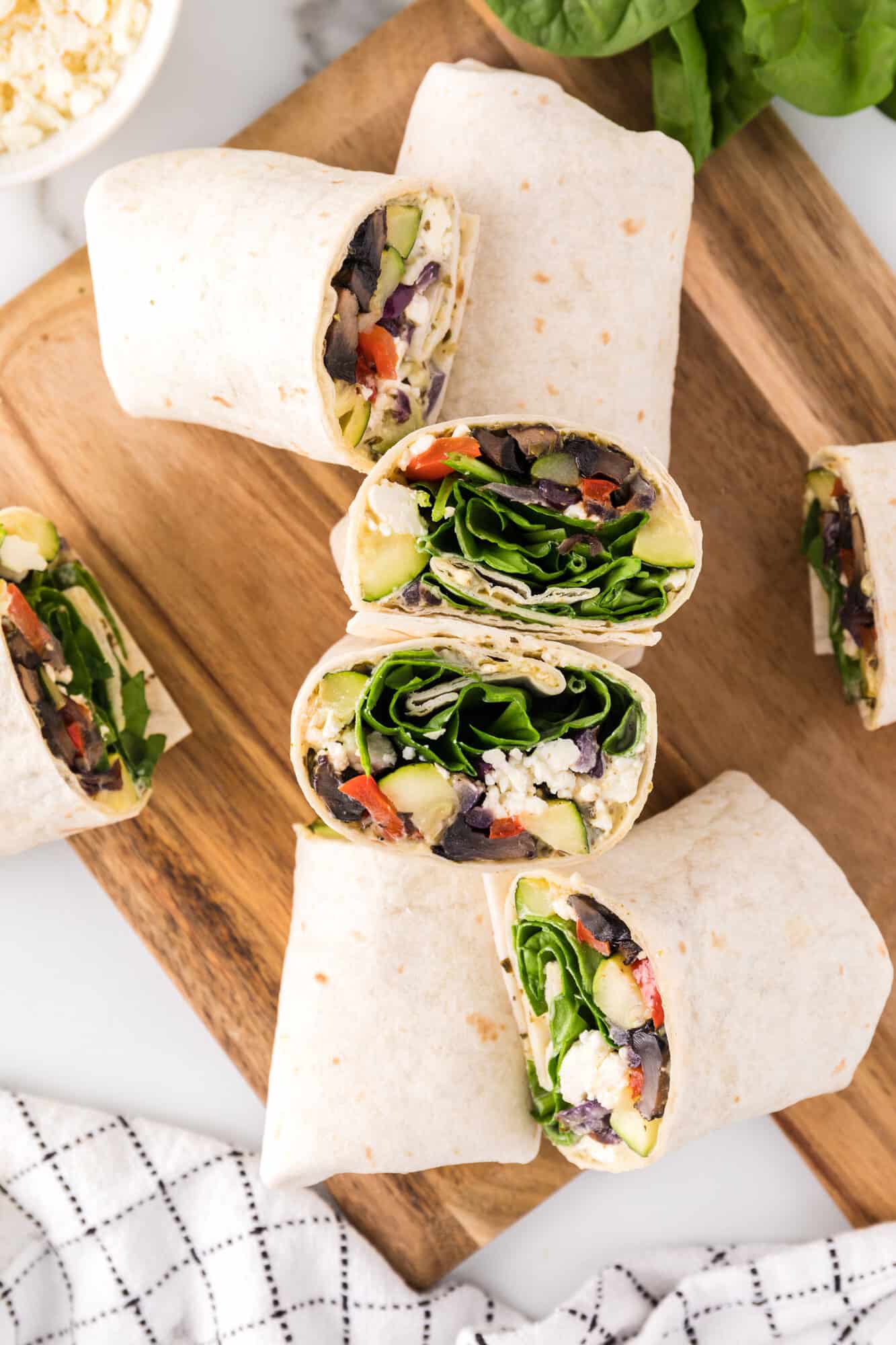 Assorted halves of roasted vegetable wraps on a wooden cutting board.