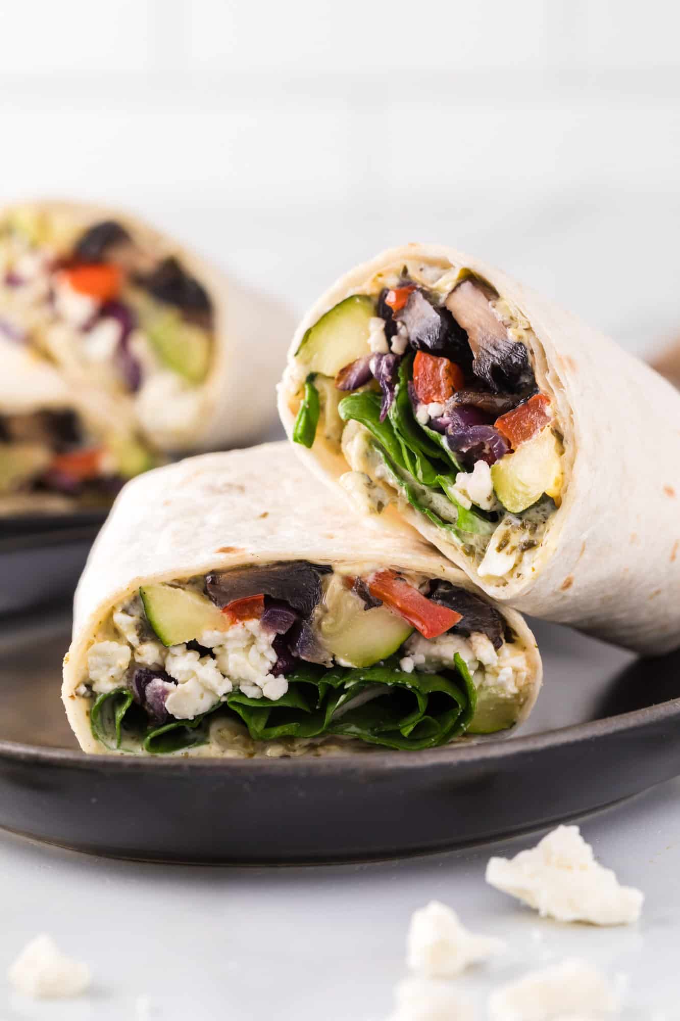 Two halves of a roasted vegetable wrap on a black ceramic plate.