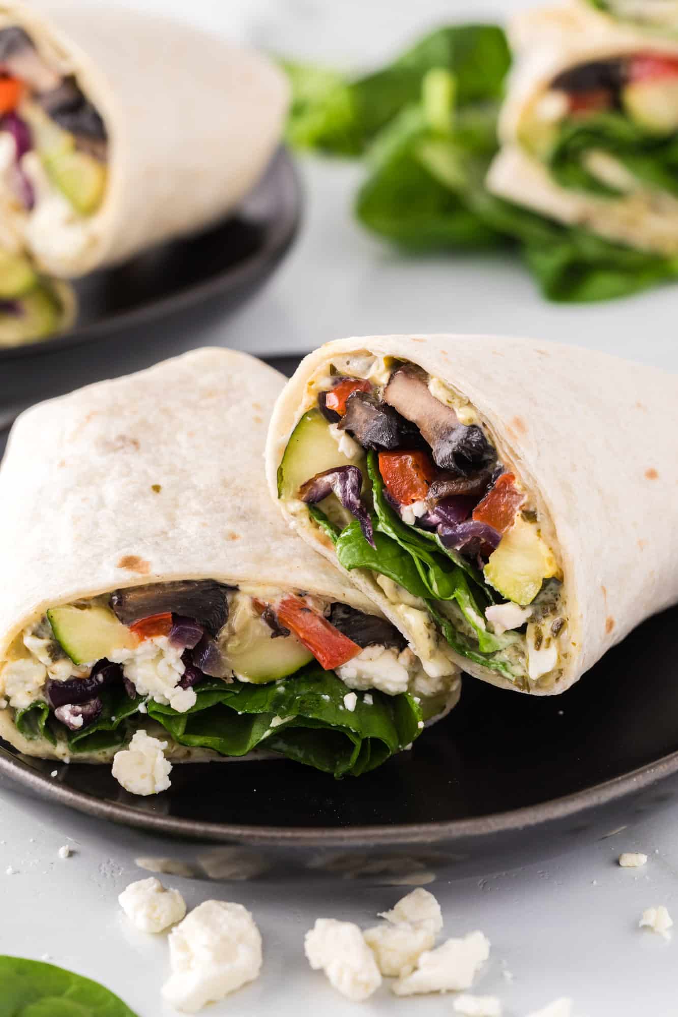 Two halves of a roasted vegetable wrap on a black ceramic plate.