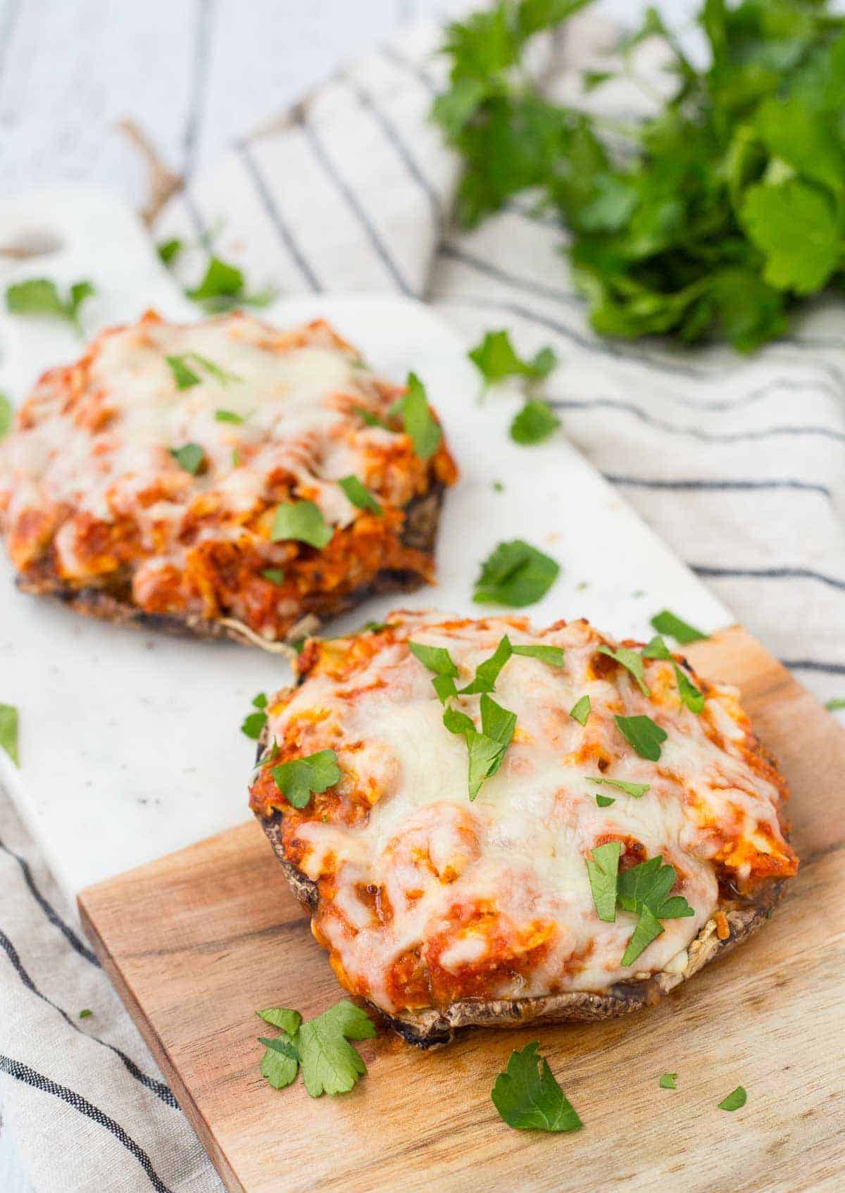 Two servings of chicken Parmesan on cutting board, garnished with chopped parsley.