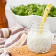 Front view of small glass jar containing poppy seed dressing and yellow spoon.