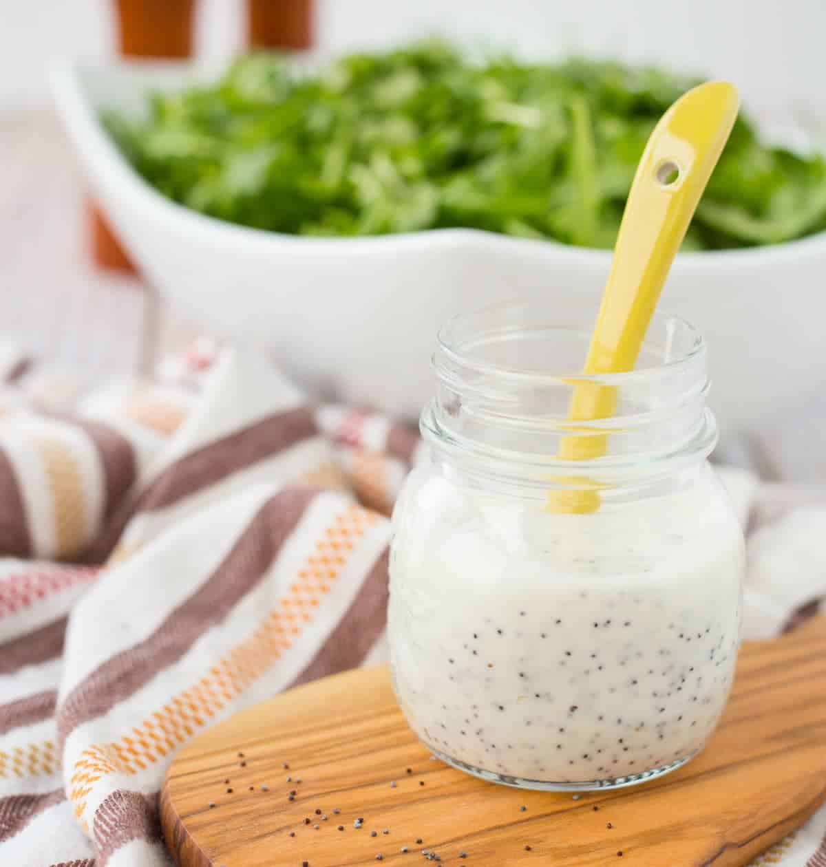 Front close up of small glass jar containing dressing and yellow spoon.