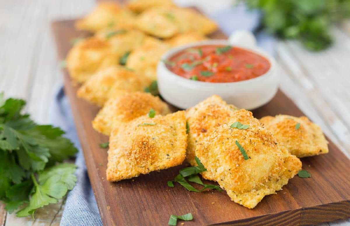 Front view of toasted ravioli on board, garnished with flat leaf parsley.