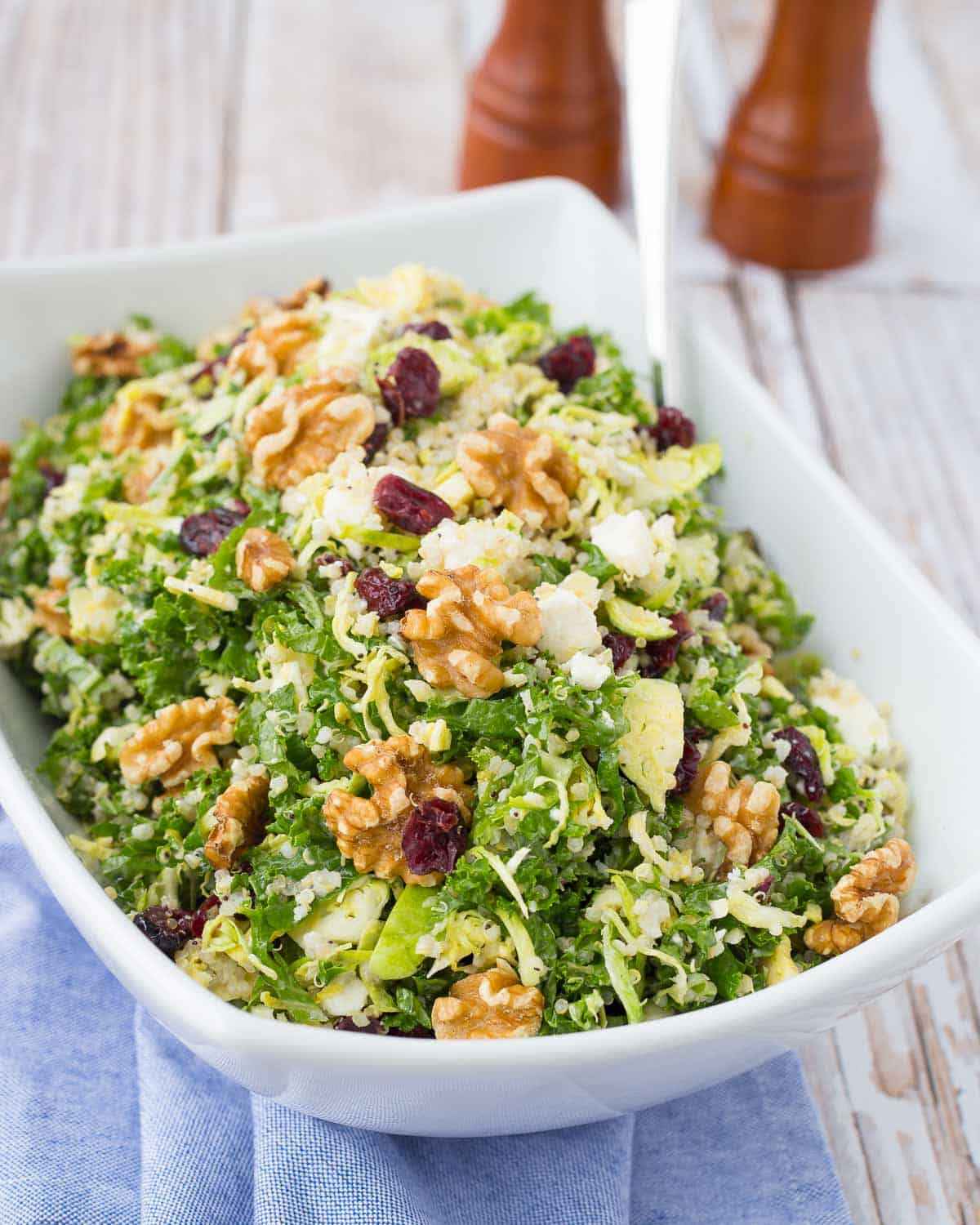 Kale salad in a large white bowl, topped with walnuts and dried cranberries.