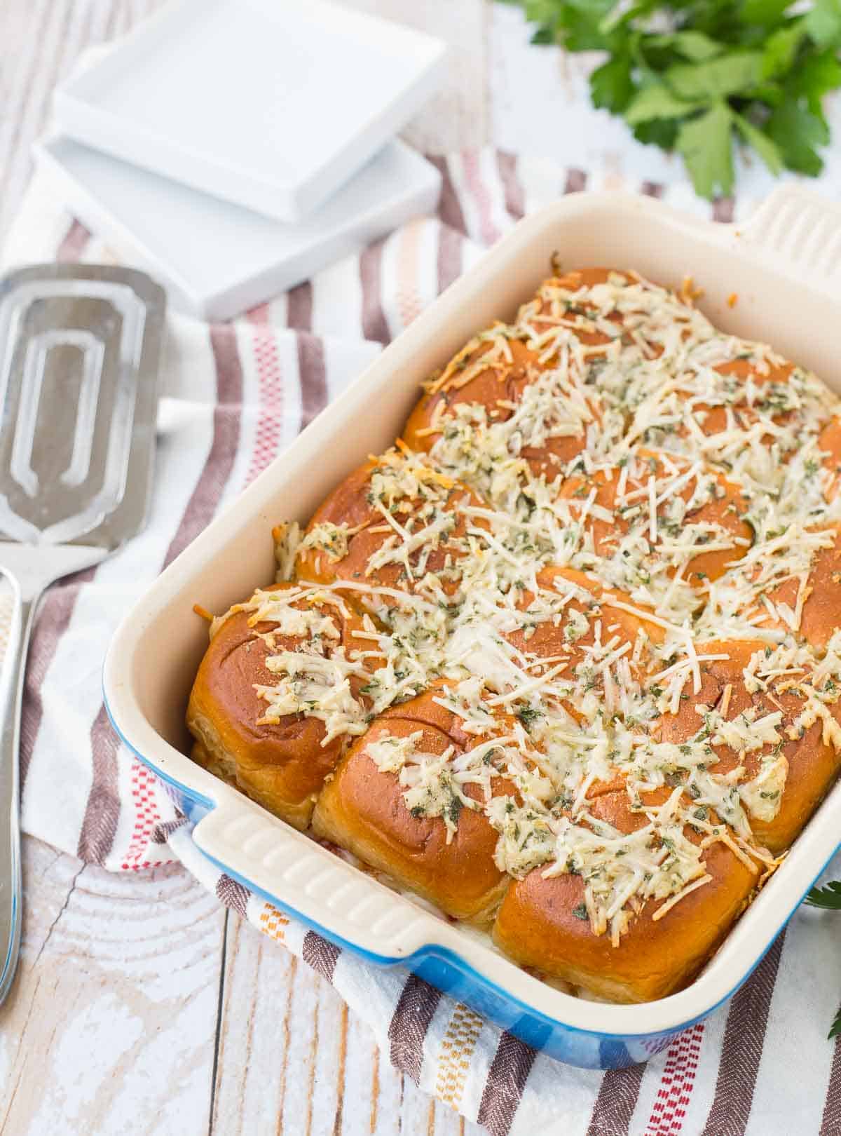 Casserole dish of pizza sliders, topped with parmesan cheese.