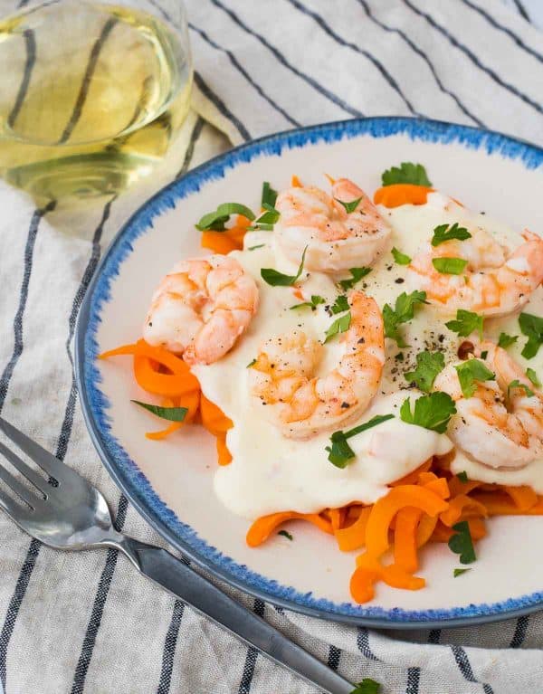 Plate of shrimp alfredo, with fork and glass of white wine, on blue striped cloth.