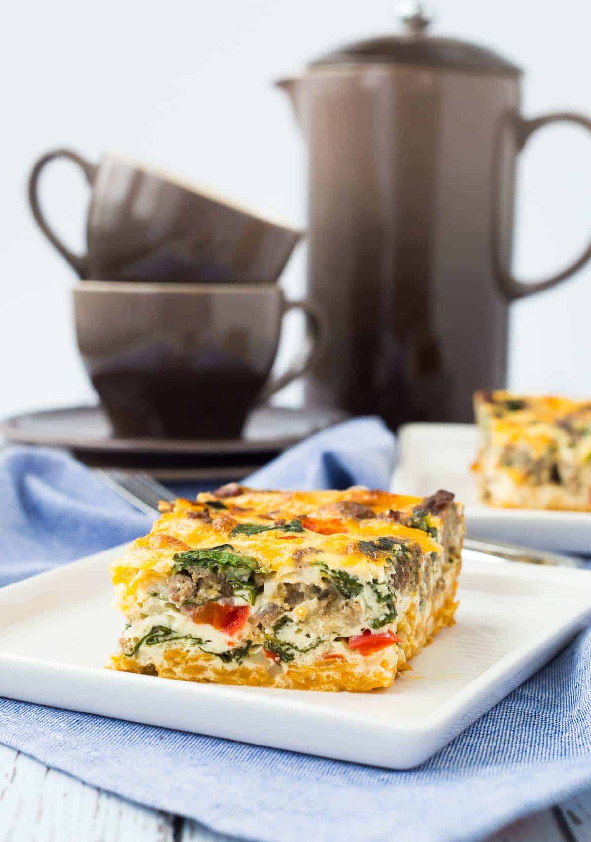 Serving of egg white casserole on square white plate with coffee in background.