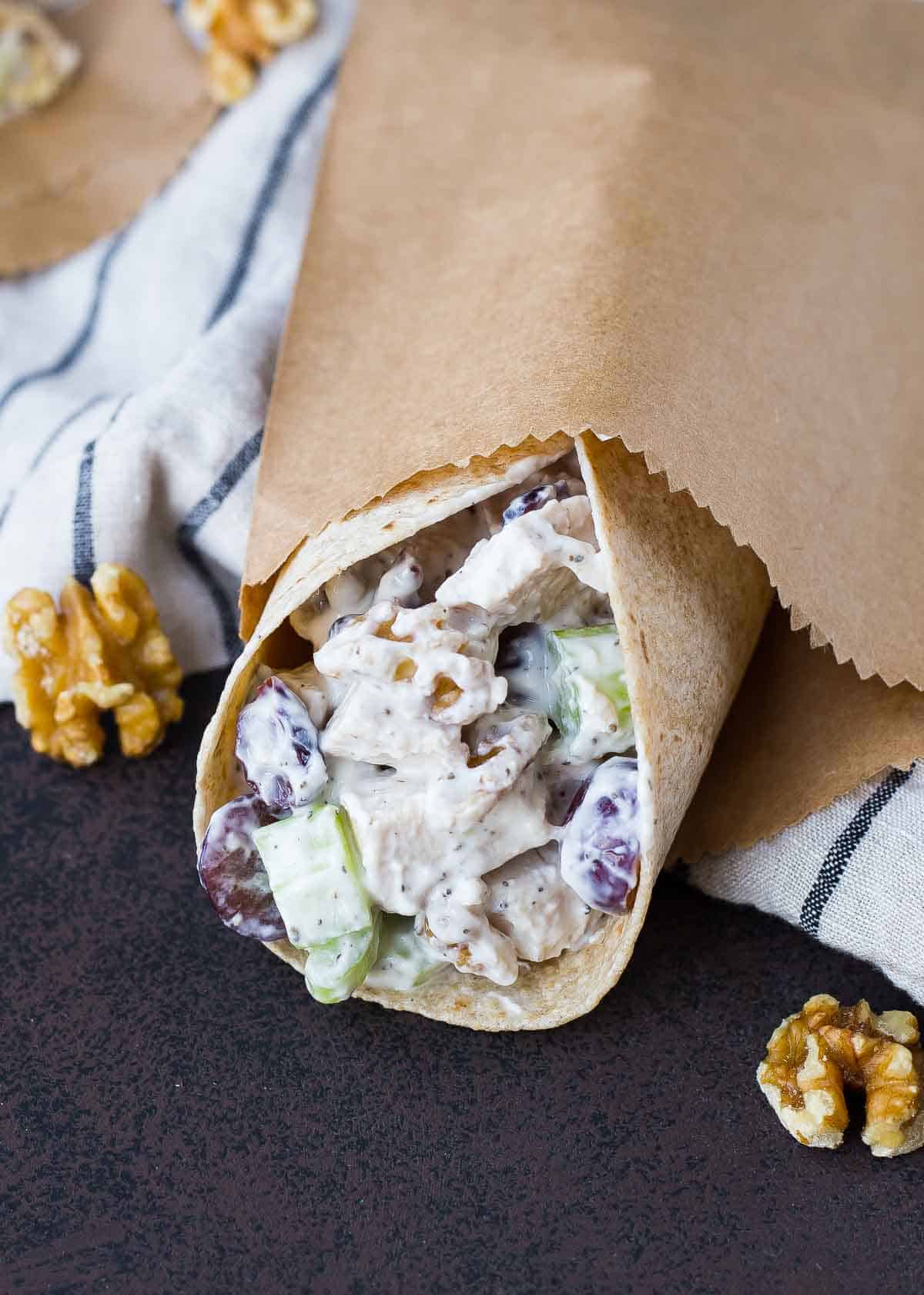 Chicken salad wrap partially contained in brown paper bag.