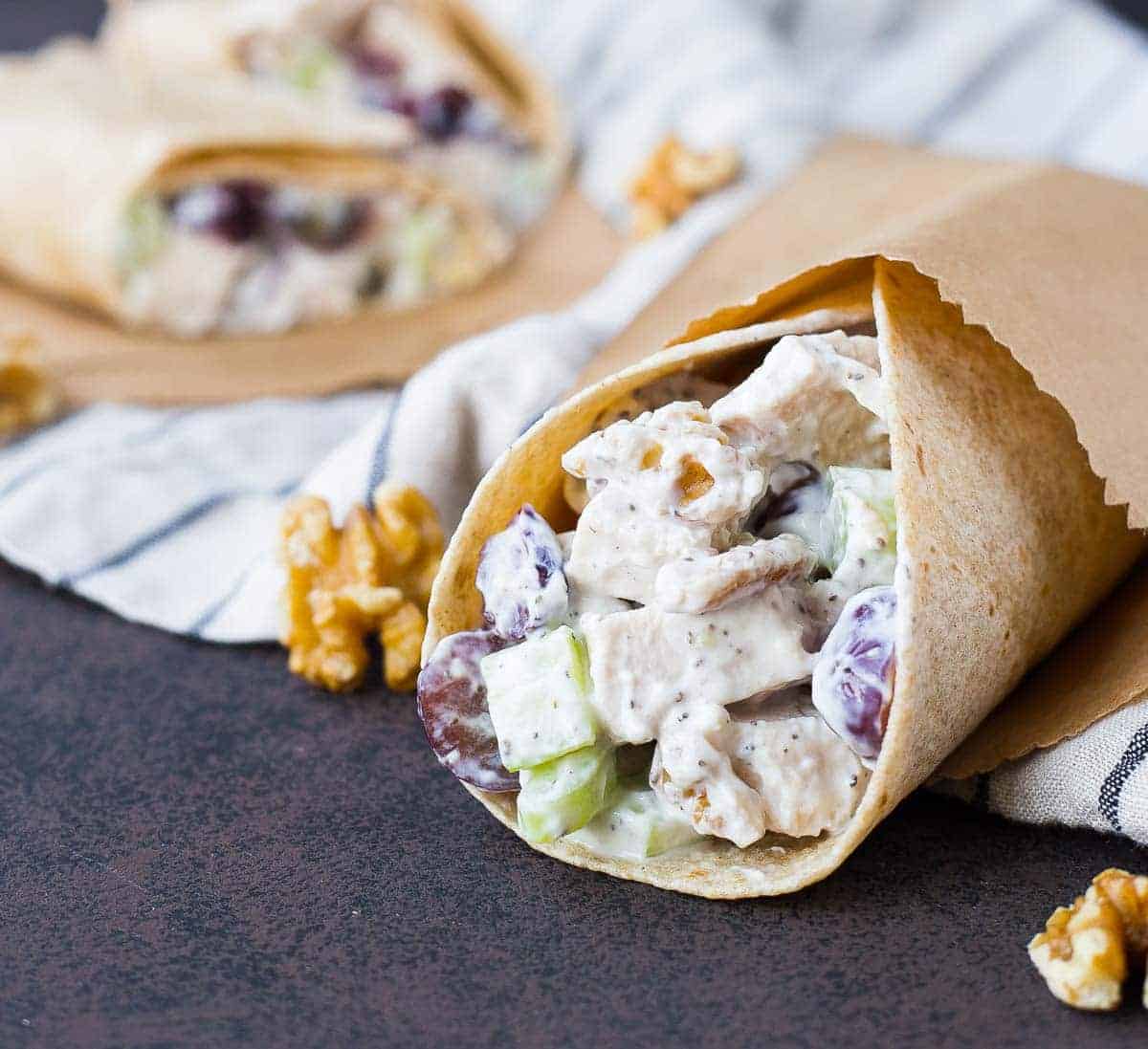 Chicken salad wrap in small brown paper bag. Walnuts scattered around.