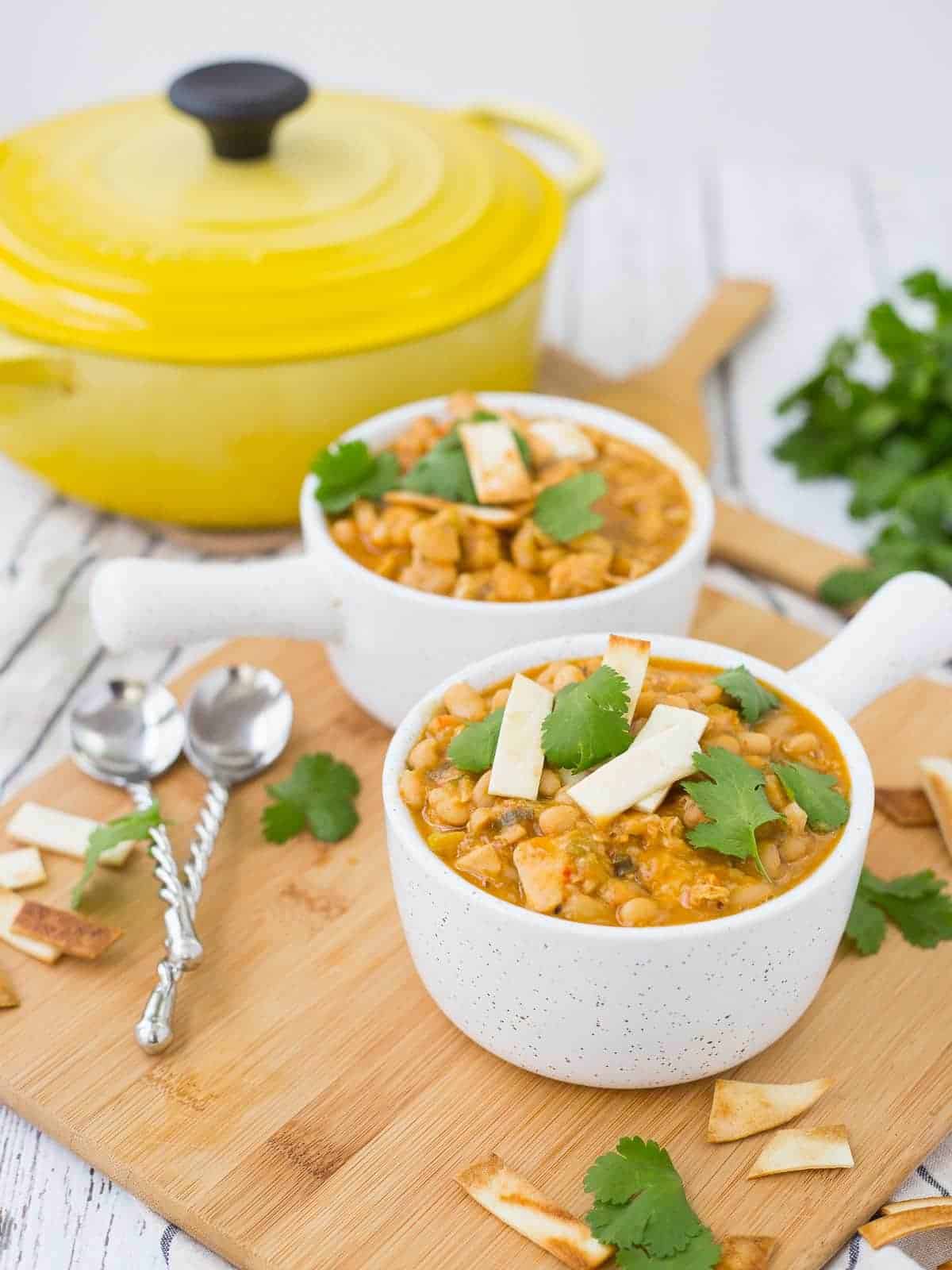 Chili in white bowls with spoons, Dutch oven in background.