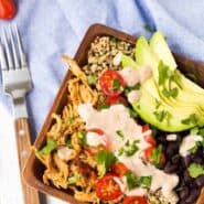 Partial image of quinoa bowl in square wooden salad bowl, with fork alongside.