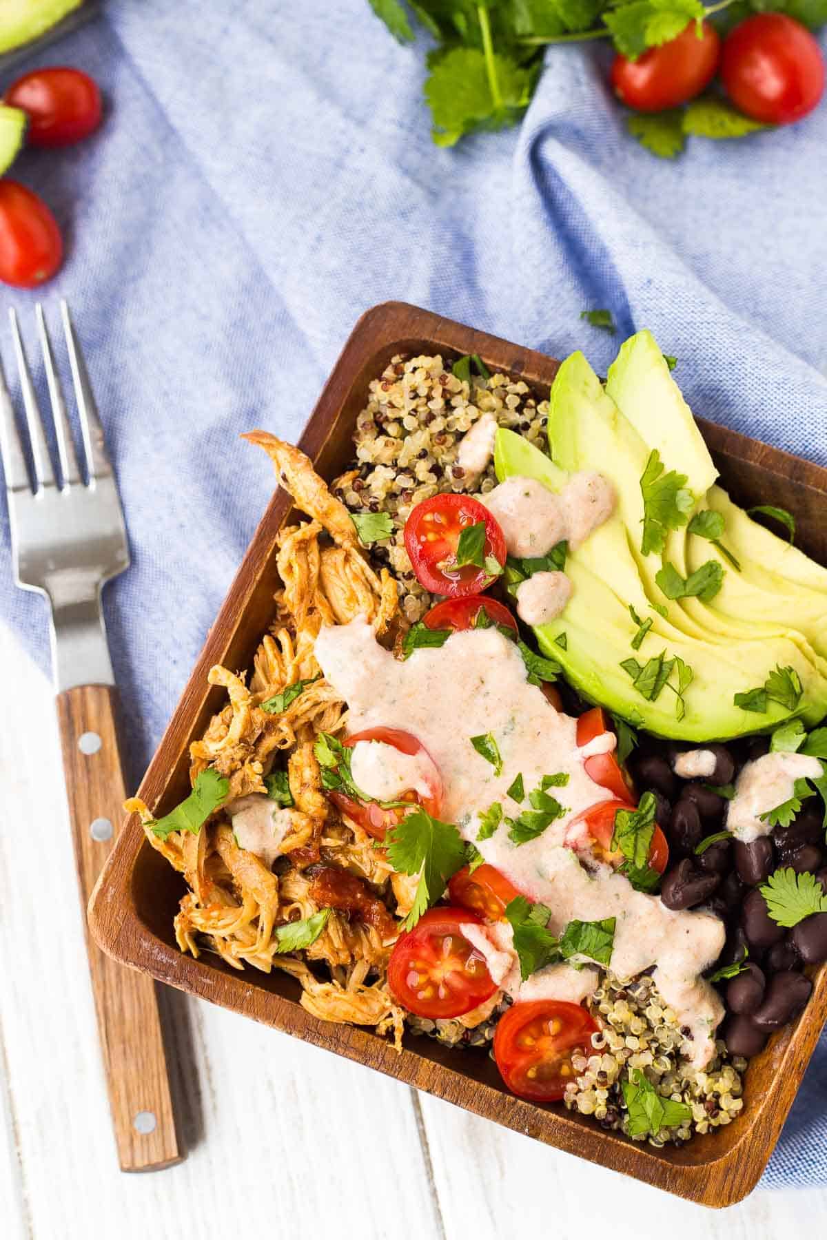 Overhead of southwestern quinoa bowl in square wooden bowl, with fork alongside.