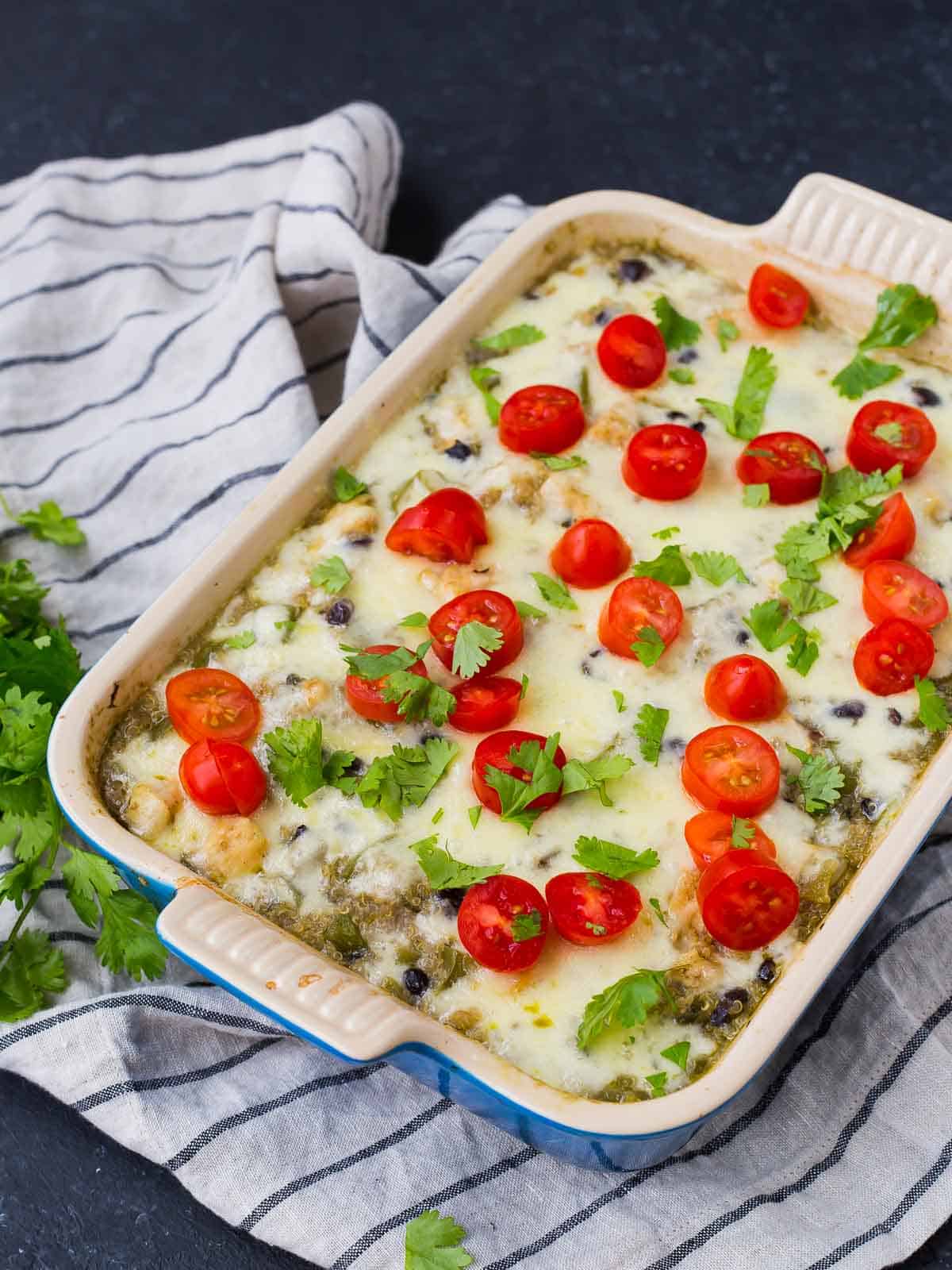 Overhead of square baking dish with casserole topped by cherry tomato halves and chopped herbs.