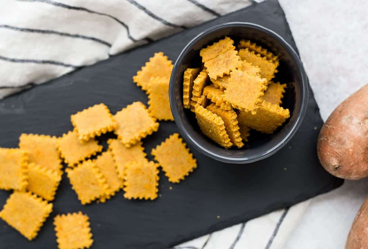 Overhead view of crackers in bowl and on black slate surface.