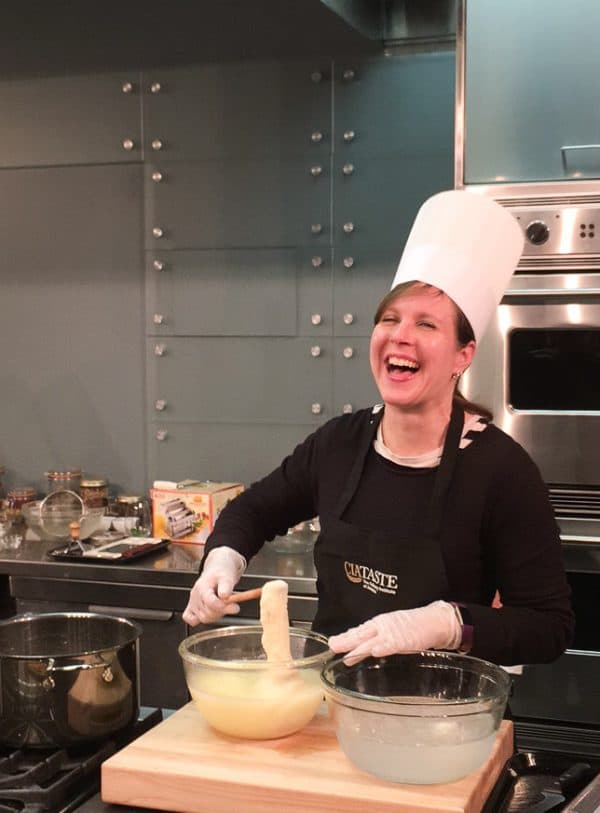A woman, laughing, with a chef's hat on, as she makes fresh mozzarella.