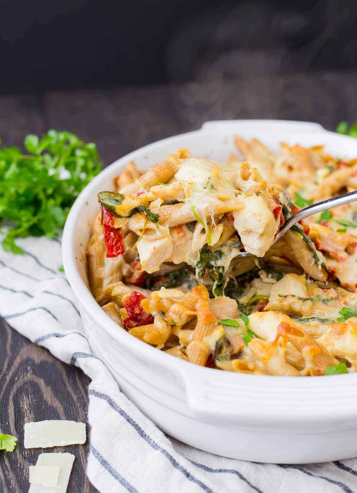 Spoon scooping out a portion of baked pasta from casserole dish.