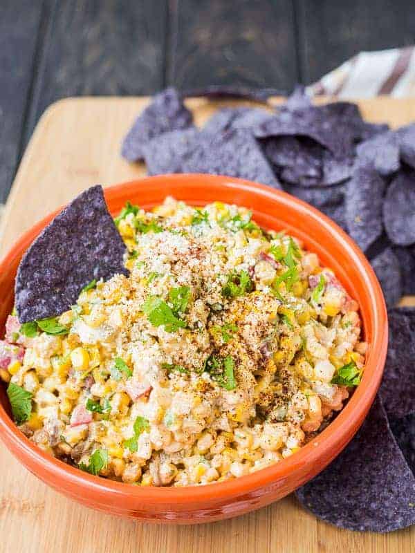 Mexican corn dip in orange bowl, surrounded with blue corn tortilla chips.