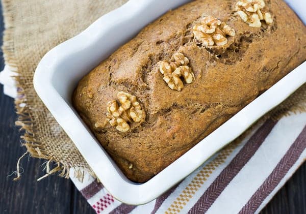 Overhead view of apple bread topped with walnuts in a white loaf pan.