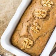 Close up of apple bread topped with walnuts in a white loaf pan.