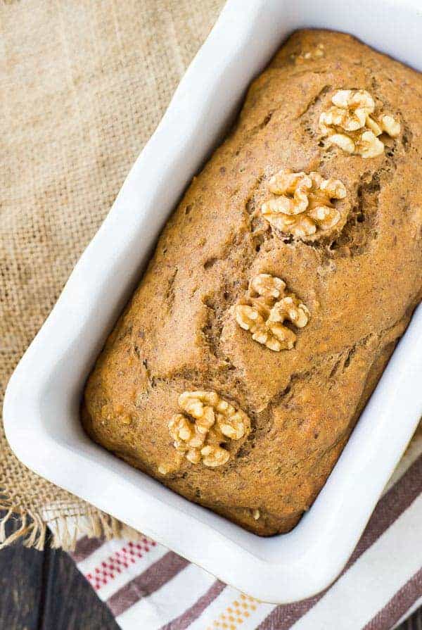 Close up of apple bread topped with walnuts in a white loaf pan.