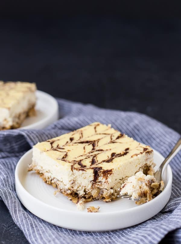 Square slice of cheesecake on round rimmed plate, placed on blue striped cloth.