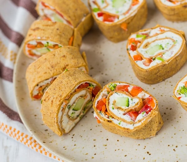 Cream cheese rolls ups with vegetables and herbs, sliced, on an earth-toned plate.