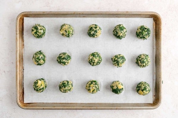 Unbaked spinach balls on a parchment-lined baking sheet.