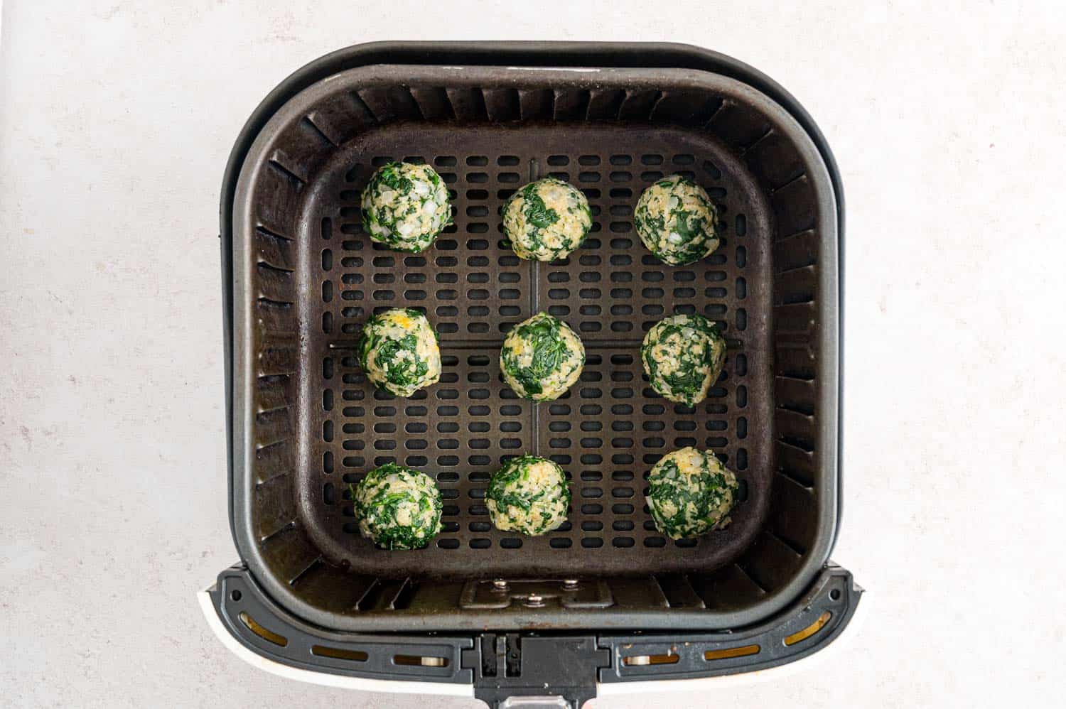 Uncooked spinach balls arranged inside the basket of an air fryer.