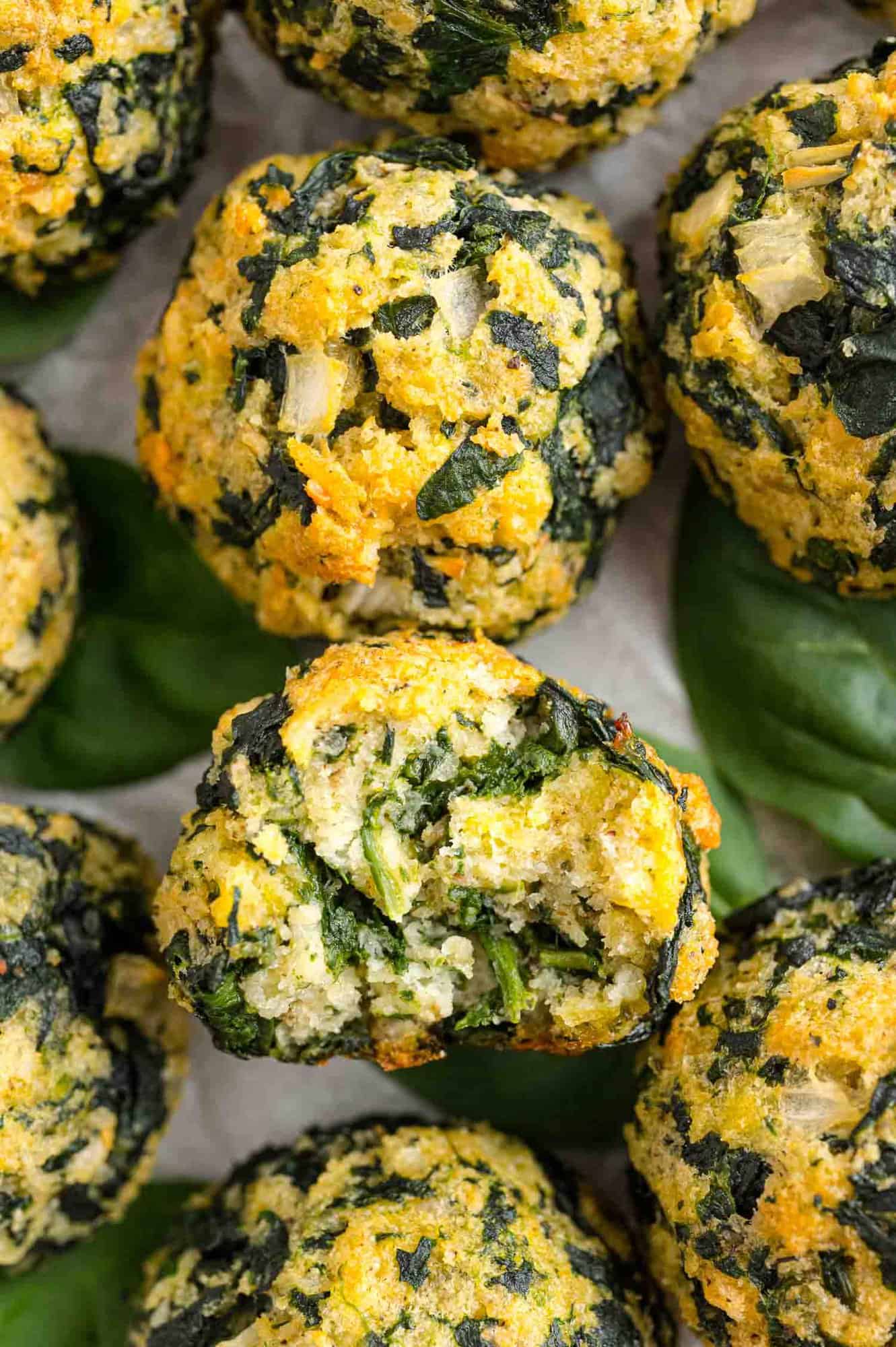 Close up overhead view of assorted spinach balls, one with a bite missing.