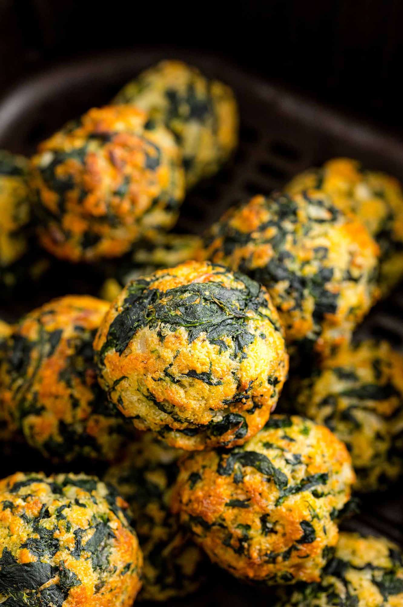 Spinach balls are great served hot from the oven or air fryer, or at room temperature, making them a perfect appetizer for any season! Close up of assorted cooked spinach balls inside the air fryer.