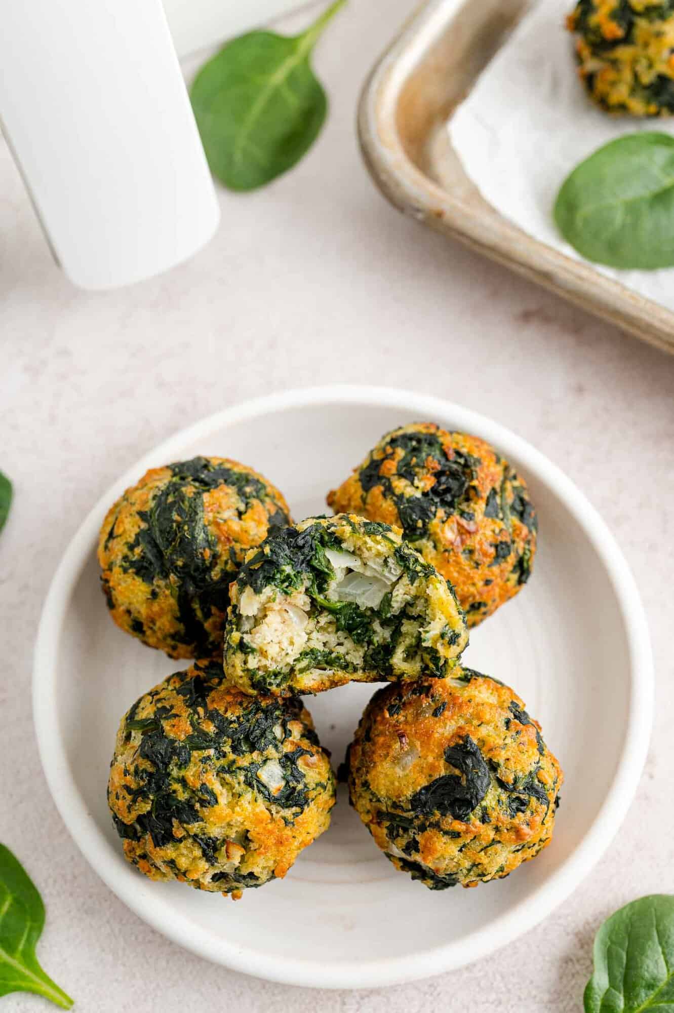 Overhead view of spinach balls stacked on a white plate, with a bite missing from the top spinach ball.