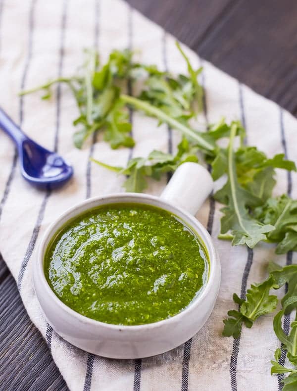 Arugula pesto in a small bowl with a blue spoon.