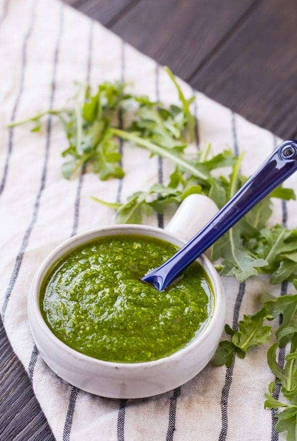 Arugula pesto in a small bowl with a blue spoon.