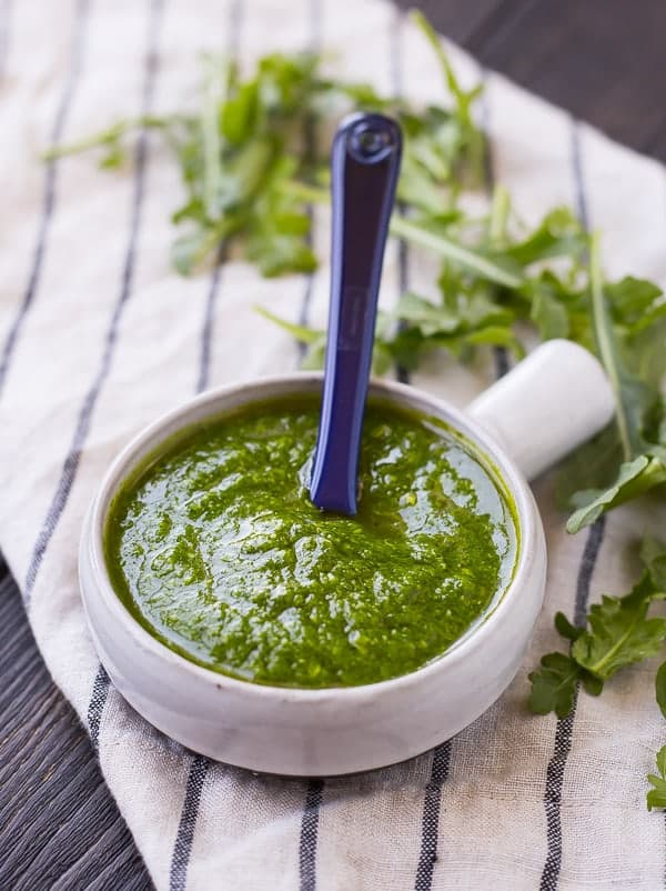 Arugula pesto in a small bowl with a blue spoon.