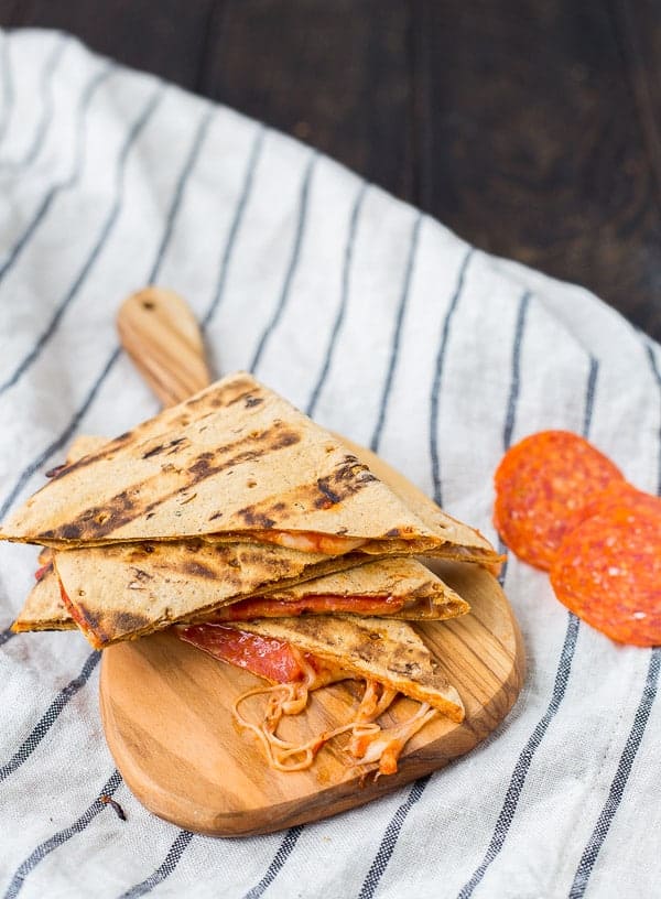 Quesadilla cut into quarters on small cutting board, with a couple pepperoni slices alongside.