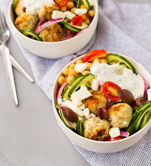 Two salads topped with tzatziki and greek meatballs.