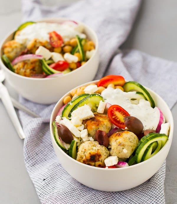 Two salads topped with meatballs in round white bowls.