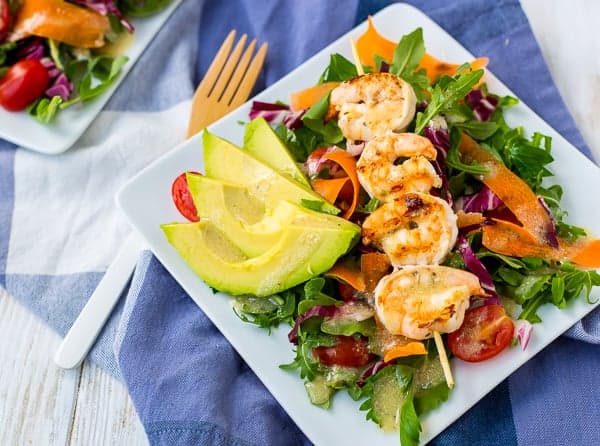 Grilled shrimp, on simple green salad with ribbons of carrot and sliced cherry tomatoes, garnished with sliced avocado.