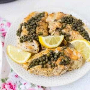 Cooked chicken on a plate with lemon slices and capers.