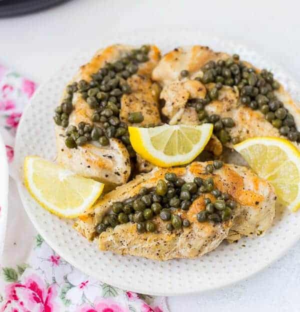 Cooked chicken on a plate with lemon slices and capers.
