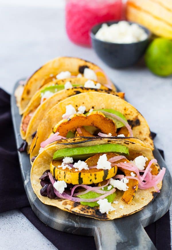 Front view of several prepared tacos on decorative cutting board, with toppings in background.