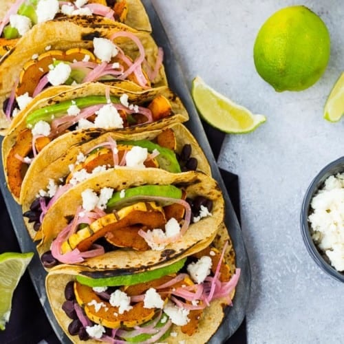 Overhead of several prepared tacos, lined up on decorative surface.