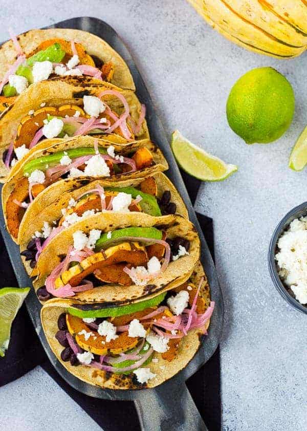 Overhead of several prepared tacos on decorative cutting board.