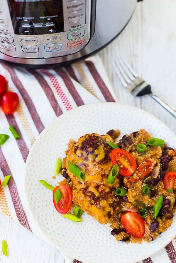 Overhead of small white plate with serving of chicken and quinoa, garnished with sliced green onions and tomatoes.