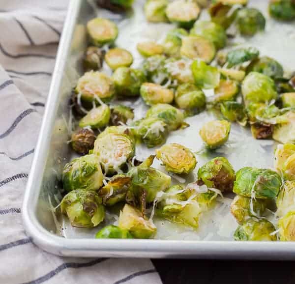 Partial view of sheet pan containing roasted Brussels sprouts, sprinkled with cheese.